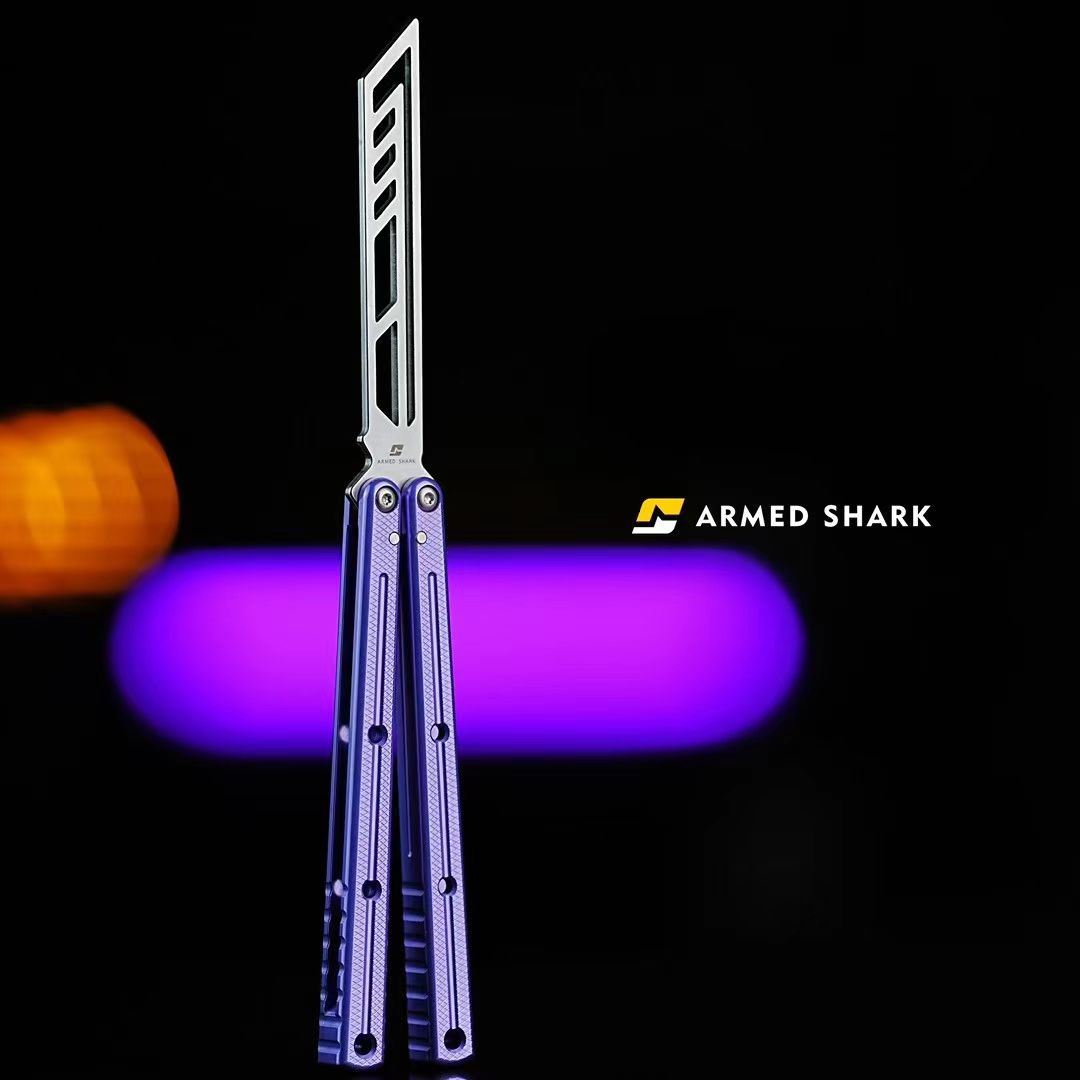 Armed Shark Krake Raken V3 balisong butterfly trainer with silver skeletonized dull blade and purple handles, displayed against a black background with purple and orange bokeh lighting.