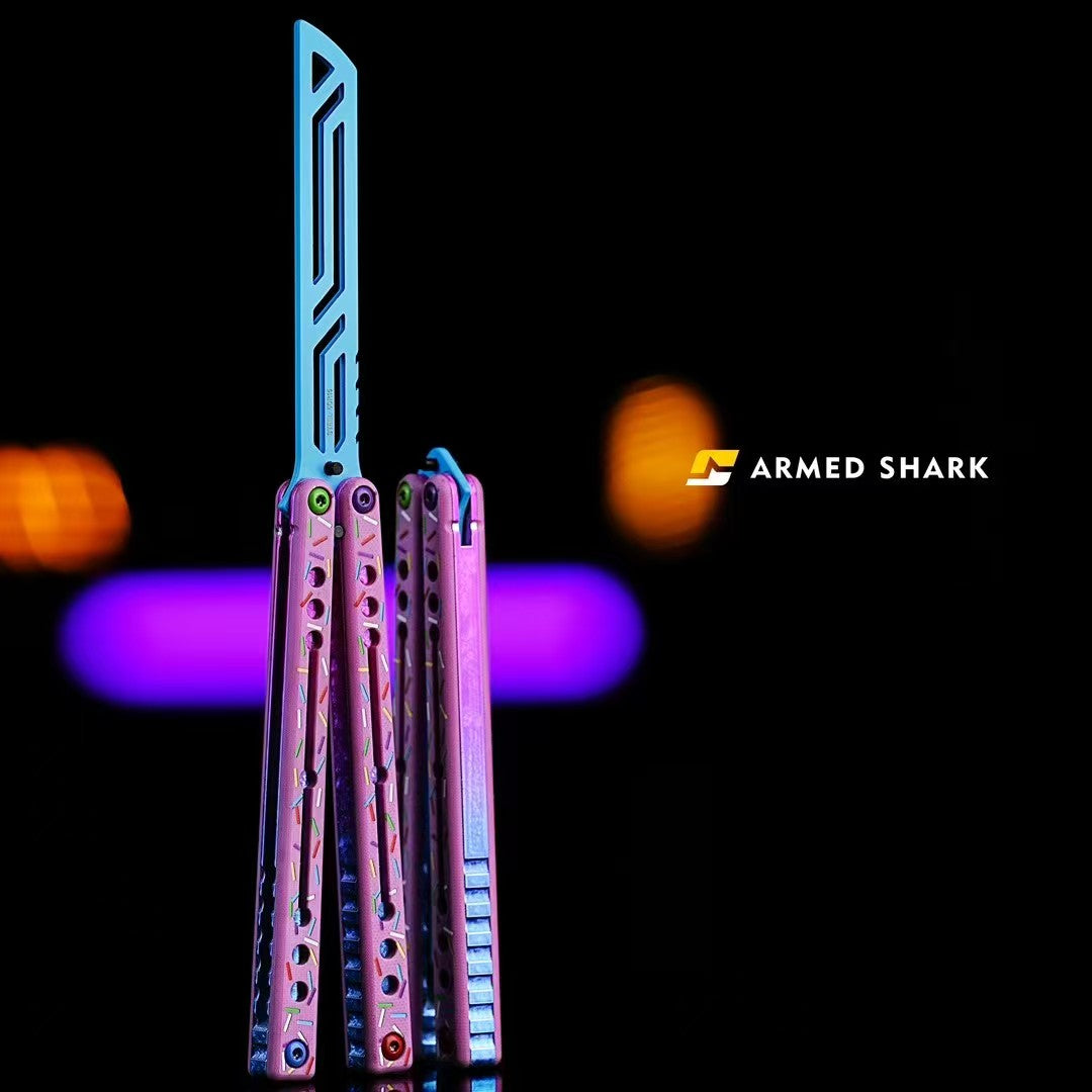 Armed Shark Nautilus V2 7075 aluminum balisong butterfly trainer in Donut colorway, featuring pink handles and a blue skeletonized dull blade, set against a black background with purple lighting.